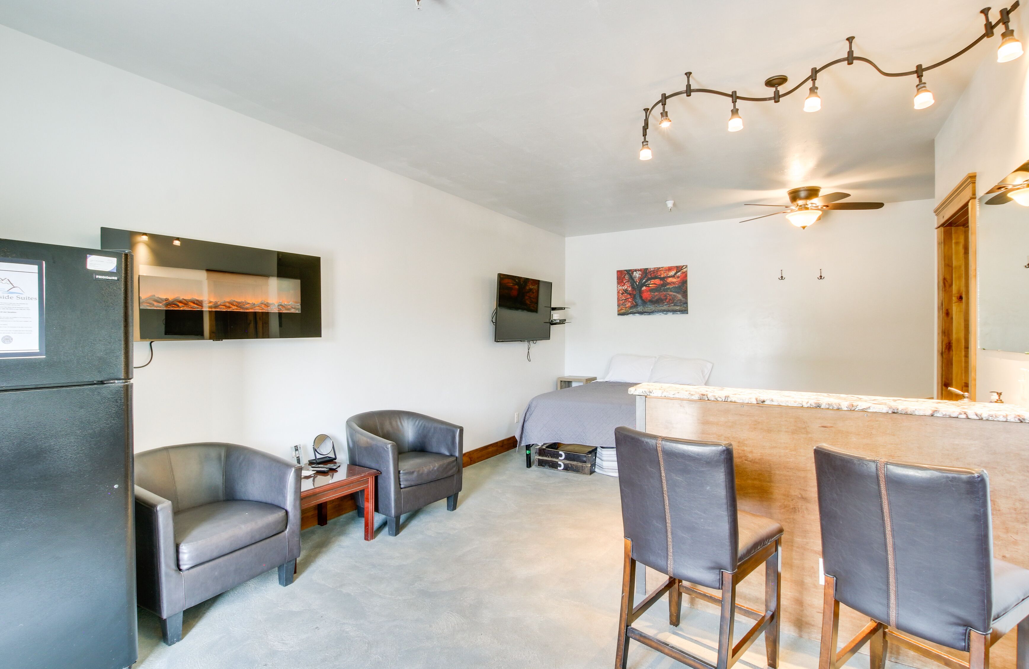 Ein kleines Hotelzimmer mit Bett, Schreibtisch, Stuhl, Kühlschrank und einem an der Wand befestigten Flachbildfernseher.