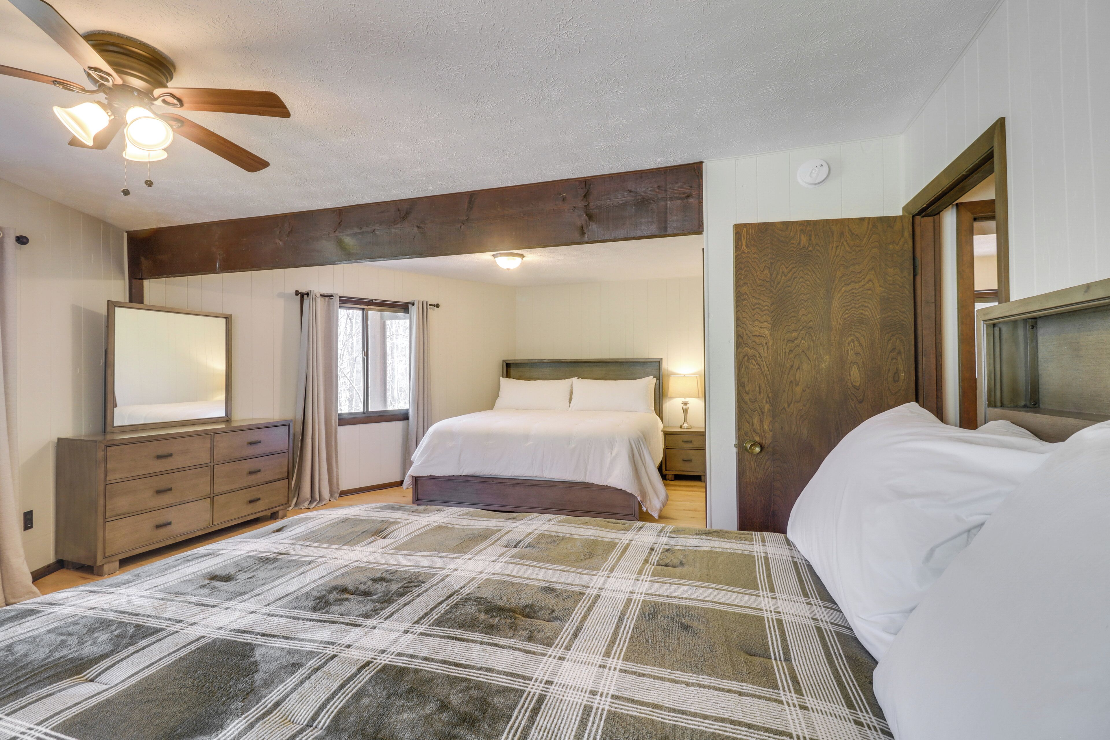 A bedroom with a bed, a dresser, a nightstand, a ceiling fan, and a door.