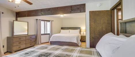 A bedroom with a bed, a dresser, a nightstand, a ceiling fan, and a door.