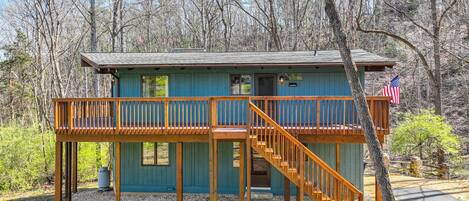A two-story cabin with a wooden deck and a staircase.