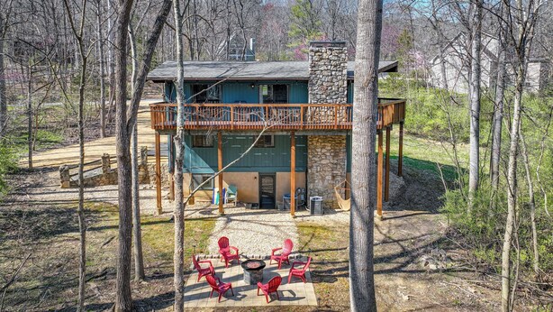A two-story building with a stone chimney, a balcony with a railing, and a patio area with red chairs and a fire pit. - Mcgaheysville Vacation Rental: Yard & Fire Pit! (McGaheysville)
