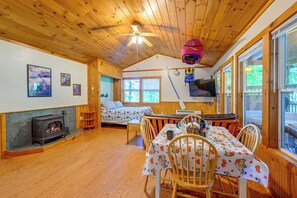 A cozy cabin interior with a wooden floor, a bed with a patterned bedspread, a dining table set for two, and a fireplace. - Cabin w/ Hot Tub - Near Nantahala Outdoor Center! (Bryson City)