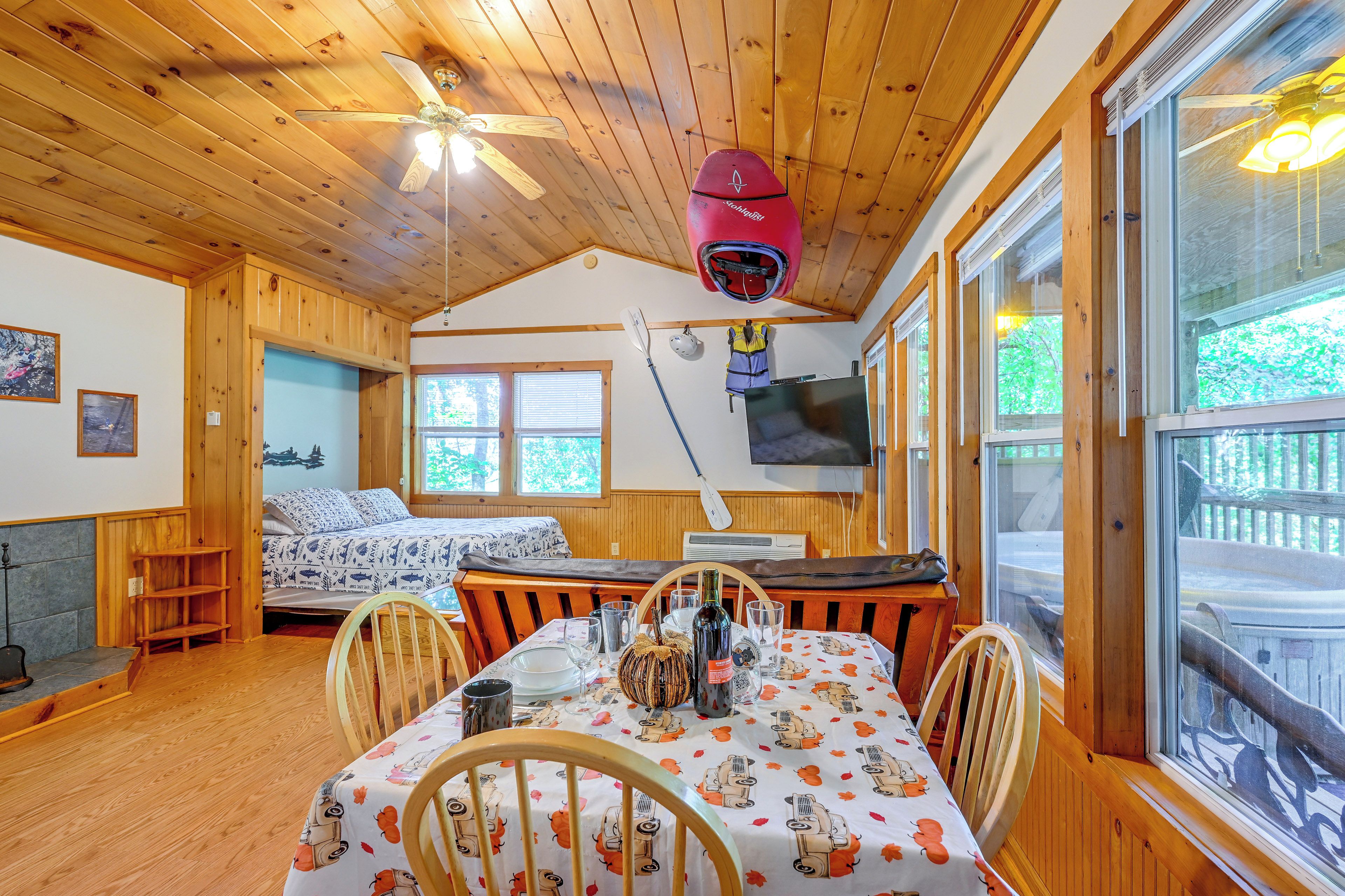 A cozy cabin interior with a dining table, chairs, a bed, and a ceiling fan.