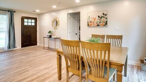 Un coin repas avec une table et des chaises en bois, une petite table d’appoint avec une plante, et une porte donnant sur une fenêtre.