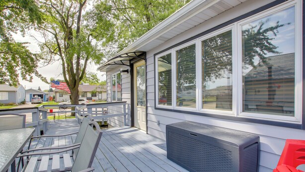 Une terrasse extérieure couverte, dotée de meubles en bois, d’une grande fenêtre et d’un radiateur de patio.