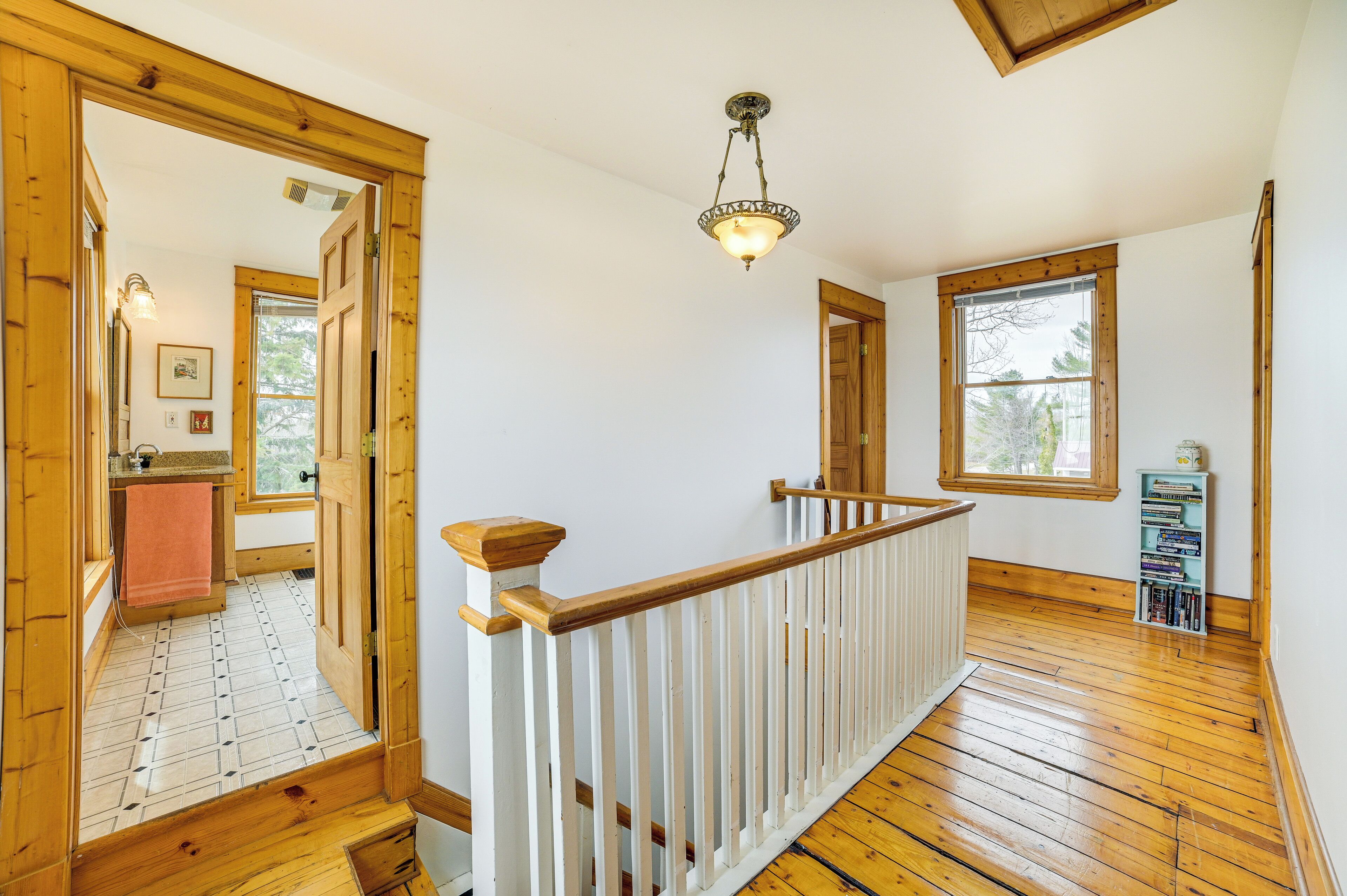A wooden staircase with a white railing leading to a landing. There is a wooden door on the landing, and a window with a view of the outdoors.