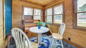 A wooden cabin interior with a round table, two chairs, a potted plant, and large windows. - Snowmobiling Hub! Mackinaw City Home 3 Mi to Beach (Mackinaw City)