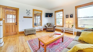 A cozy living room with wooden floors, a sofa, a coffee table, and a TV mounted on the wall. - Snowmobiling Hub! Mackinaw City Home 3 Mi to Beach (Mackinaw City)
