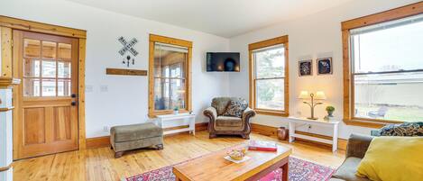 A living room with a wooden floor, a sofa, a coffee table, a chair, a TV, and a window with a view.