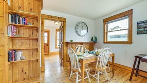 A wooden dining area with a table and chairs, a bookshelf, a clock, and a window with a view. - Snowmobiling Hub! Mackinaw City Home 3 Mi to Beach (Mackinaw City)