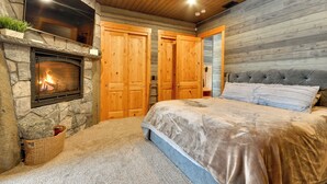 A bedroom with a stone fireplace, wooden doors, a large bed, and a ceiling with wooden beams. - Luxurious Waterfront Retreat w/ Private Pond! (Ridgefield)
