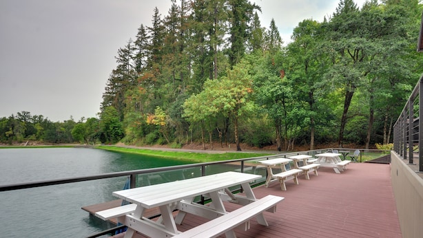A deck with picnic tables overlooking a lake, surrounded by dense trees. - Luxurious Waterfront Retreat w/ Private Pond! (Ridgefield)