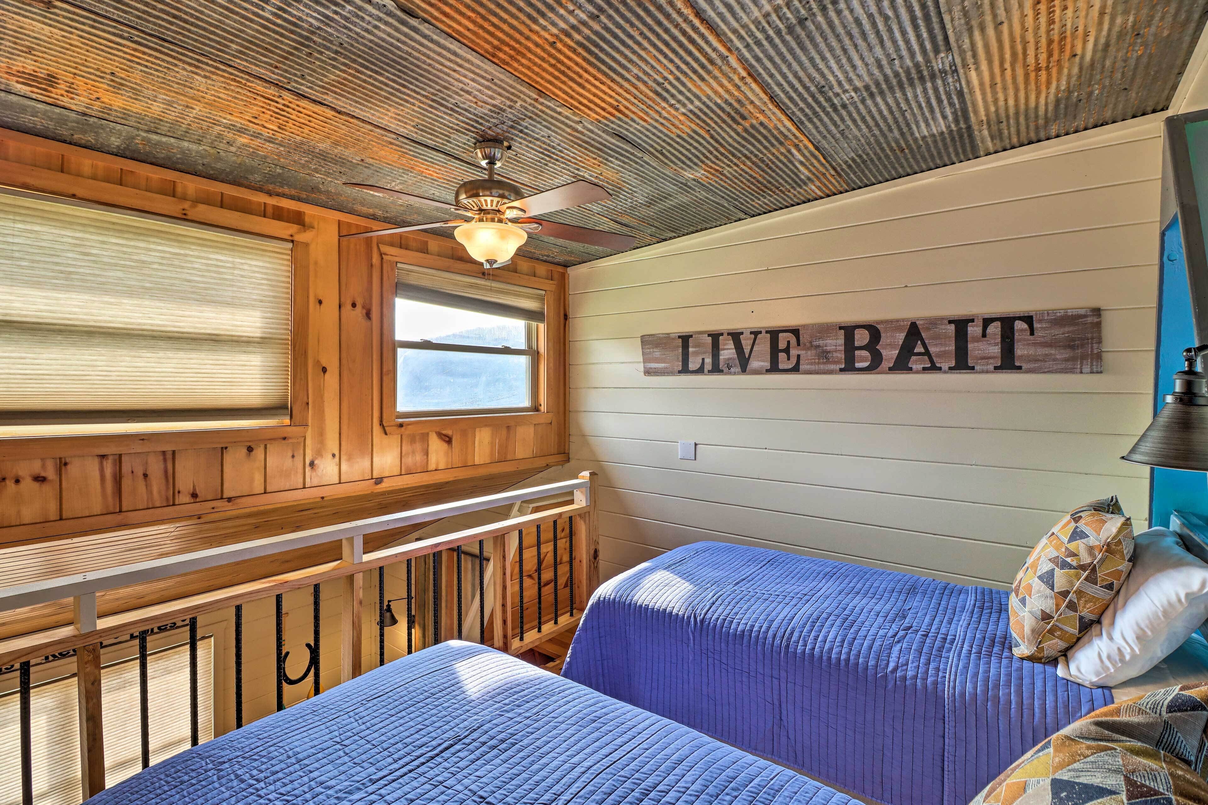 Ein Zimmer mit zwei Betten, einem Deckenventilator, einem Fenster mit Jalousien und einem Wandzeichen mit der Aufschrift 'LIVE BAIT'.