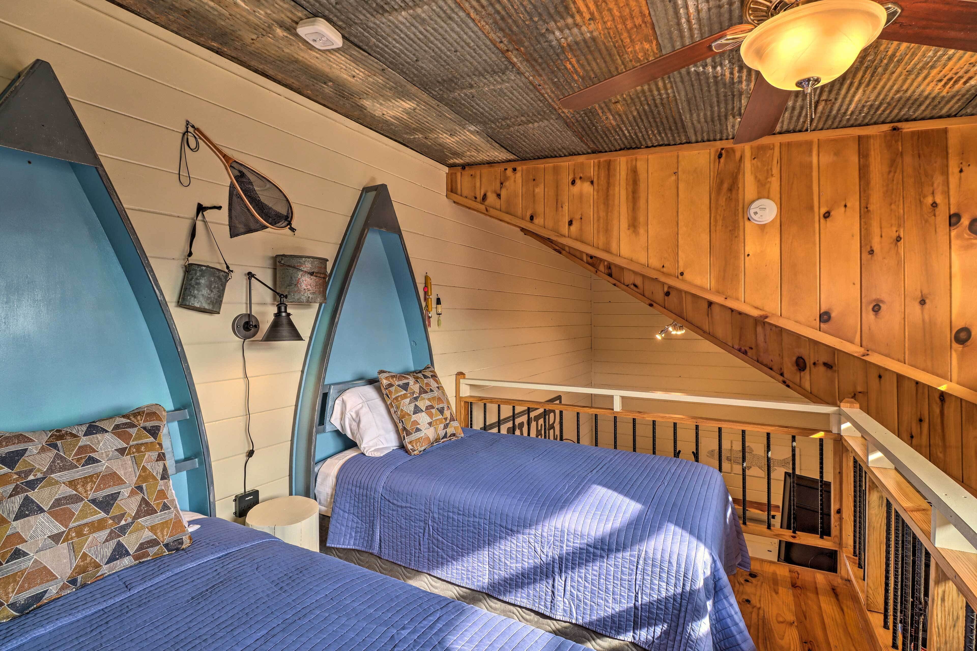 A bedroom with two beds, wooden walls, a sloped ceiling, and a small table with a lamp.
