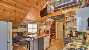 Un intérieur de chalet chaleureux comprenant une cuisine, un coin repas et une chambre à coucher située en mezzanine.