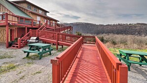 Une terrasse en bois avec des tables de pique-nique, un escalier rouge et une vue sur une colline boisée.