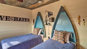 Une chambre avec deux lits, chacun doté d’une tête de lit bleue et d’oreillers à motifs. Une pancarte sur le mur indique : « E Bait ».