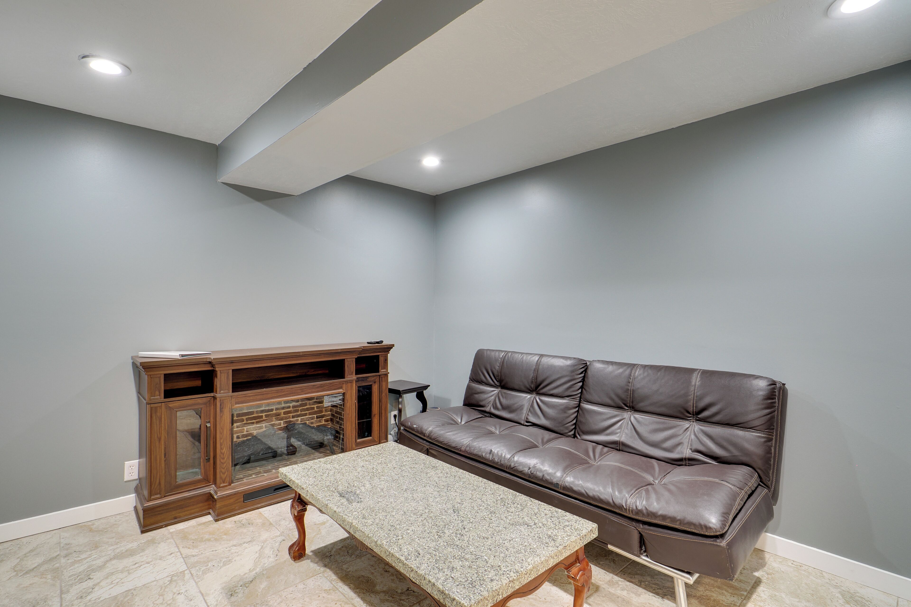 A living room with a brown leather sofa, a wooden entertainment center, and a granite coffee table.