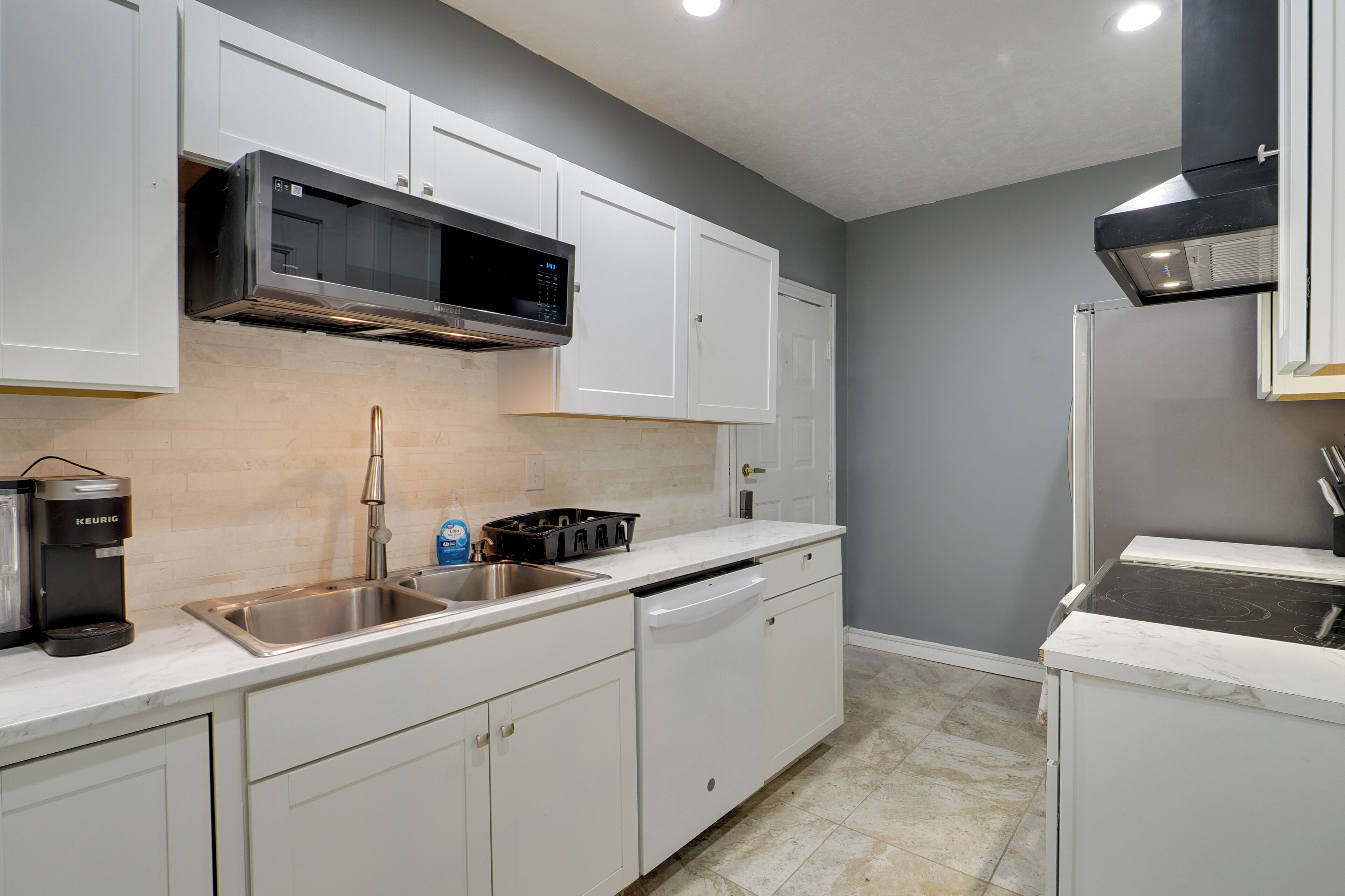 A kitchen with white cabinets, a stainless steel sink, a microwave, a coffee maker, and a stove.