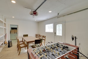 Una habitación con mesa de fútbol de mesa, una mesa de comedor, sillas, zona de cocina y proyector en el techo.