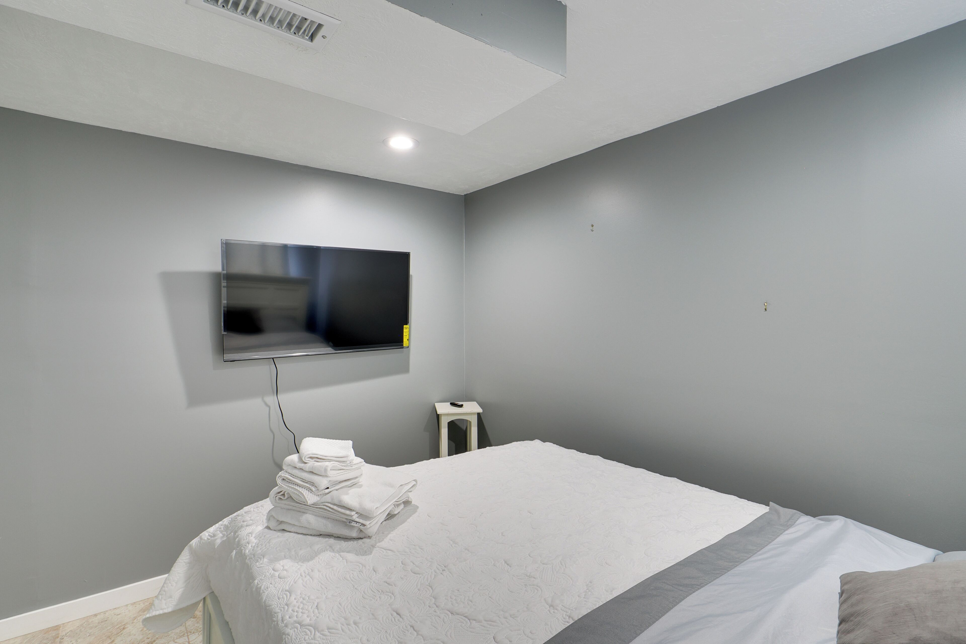 A bedroom with a bed, a TV mounted on the wall, and a small table with folded towels.