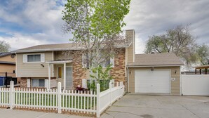 Une maison à deux étages avec un garage, une clôture blanche en bois et un petit arbre dans le jardin.
