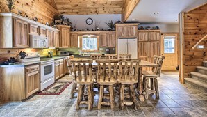 A rustic kitchen with wooden cabinets, a central island, and a dining area with wooden chairs. - Phelps Cabin on 26 Acres w/ Fire Pit! (Phelps)