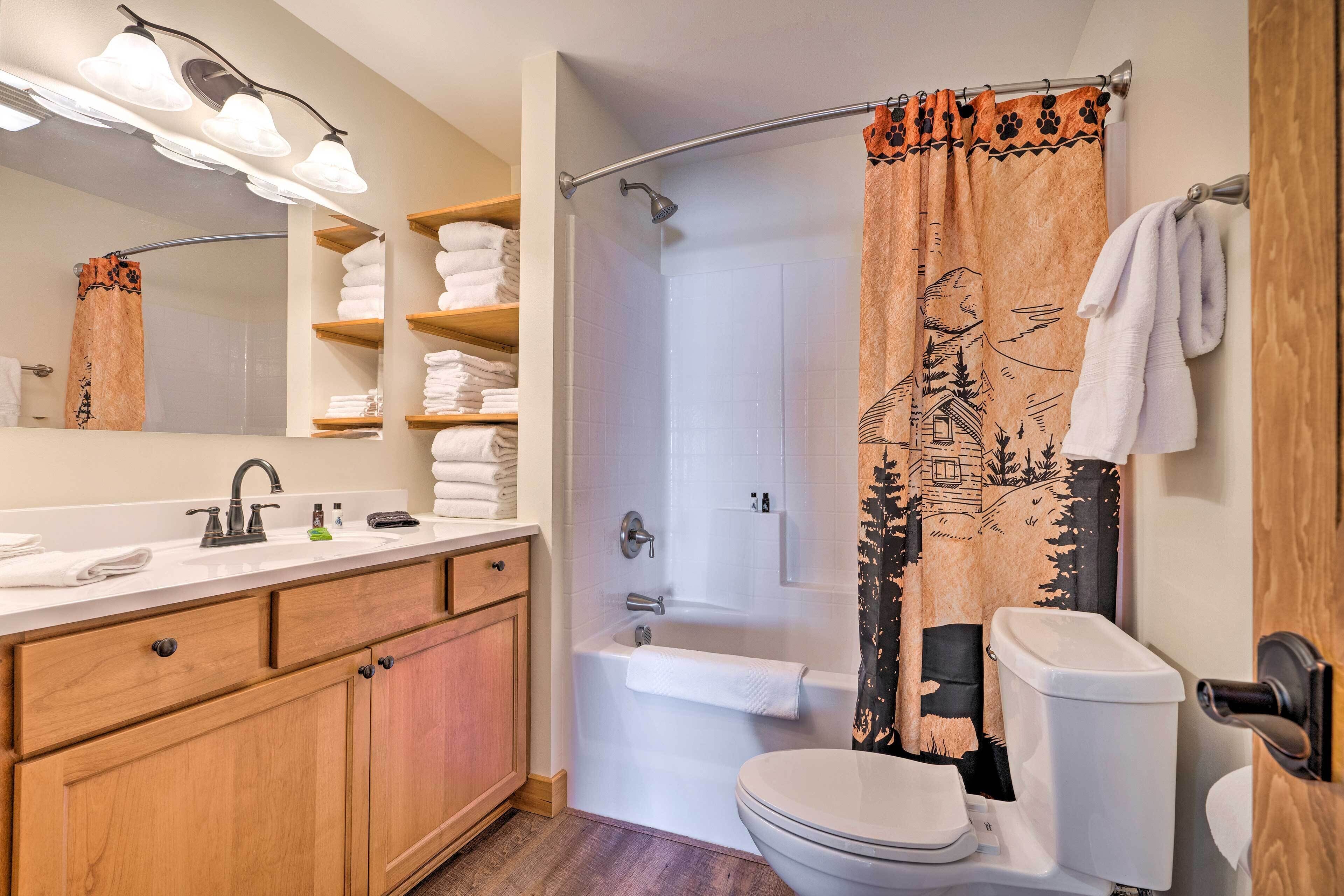 A bathroom with a wooden vanity, white sink, and a shower curtain with a forest design.