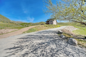 Ein Haus mit einem Feldweg, der davor hindurchführt, umgeben von Hügeln und vereinzelter Vegetation.