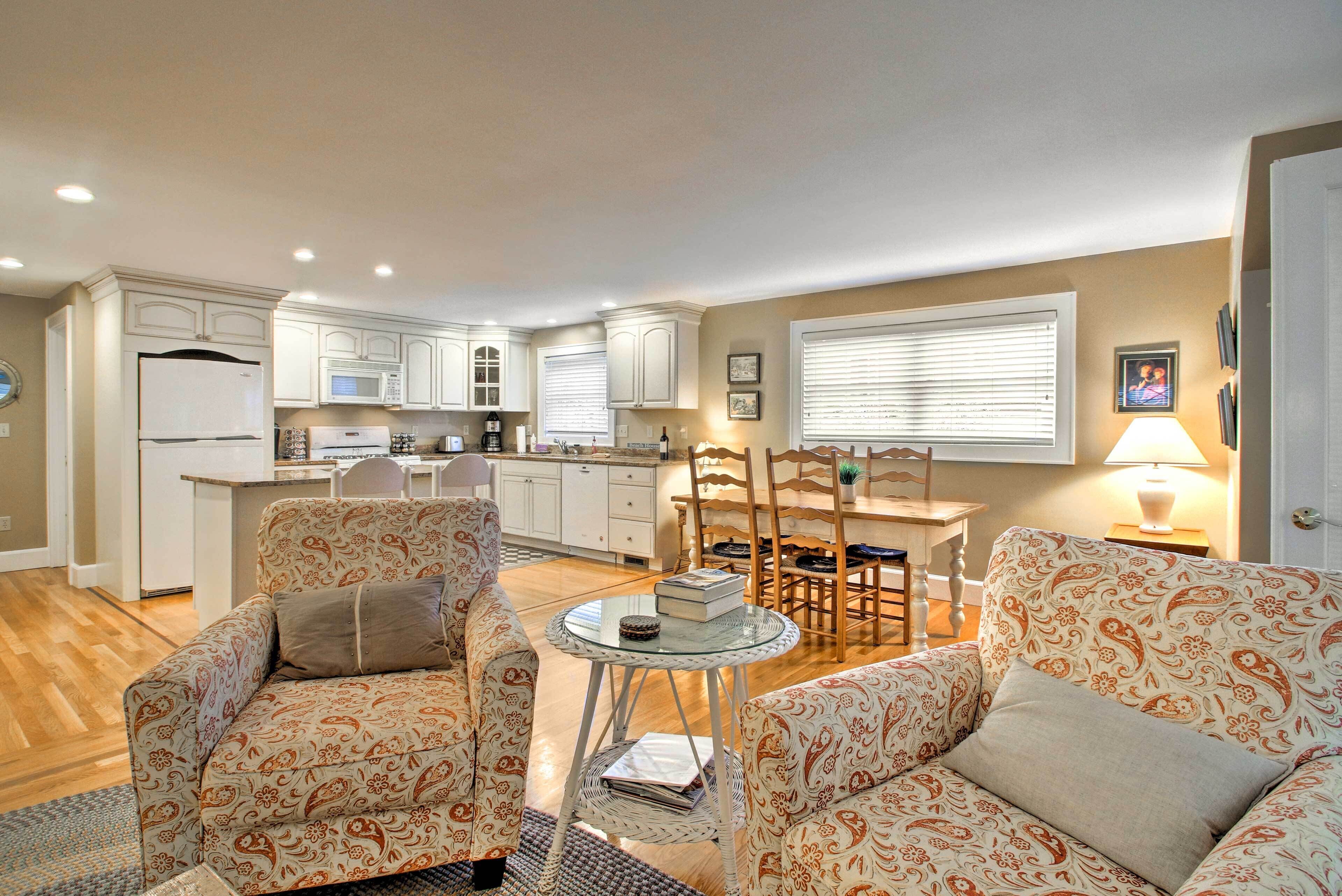 A compact living space with a kitchenette, two patterned sofas, a small dining table, and a lamp.