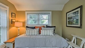 Ein Schlafzimmer mit Bett, Nachttisch, Lampe, Fenster und einem Bild an der Wand.