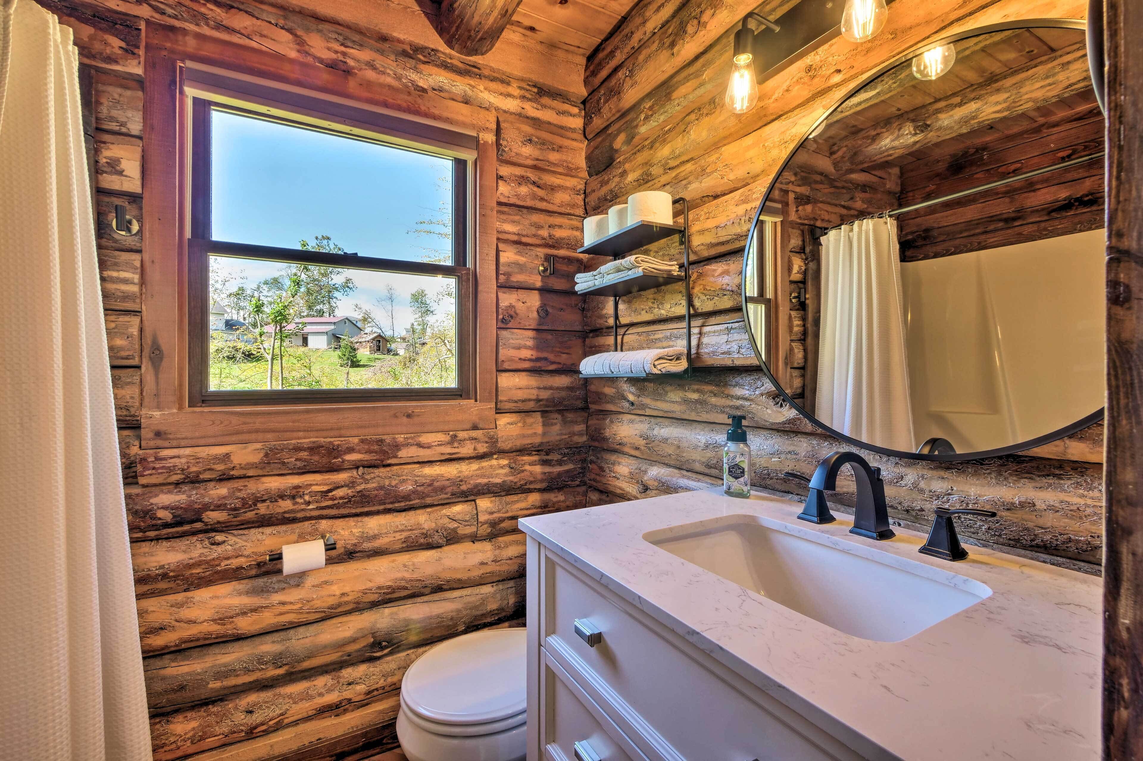 A rustic bathroom with wooden walls, a window, a sink, and a mirror.