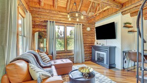 L’intérieur d’une cabane en rondins, avec un canapé en cuir, une cheminée, un téléviseur et un plafond en bois.