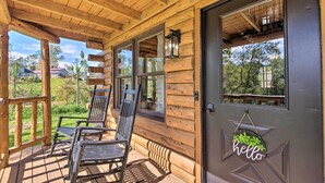 Une cabane en bois avec une véranda, une pancarte sur laquelle on peut lire « Bonjour », et une vue sur le paysage environnant.