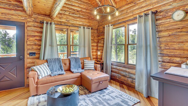 L’intérieur d’une cabane en rondins, avec un canapé en cuir, un pouf et un coin repas.