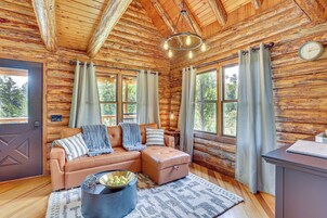 Interior de cabana de madeira com sofá de couro, apoio para os pés e área de jantar.