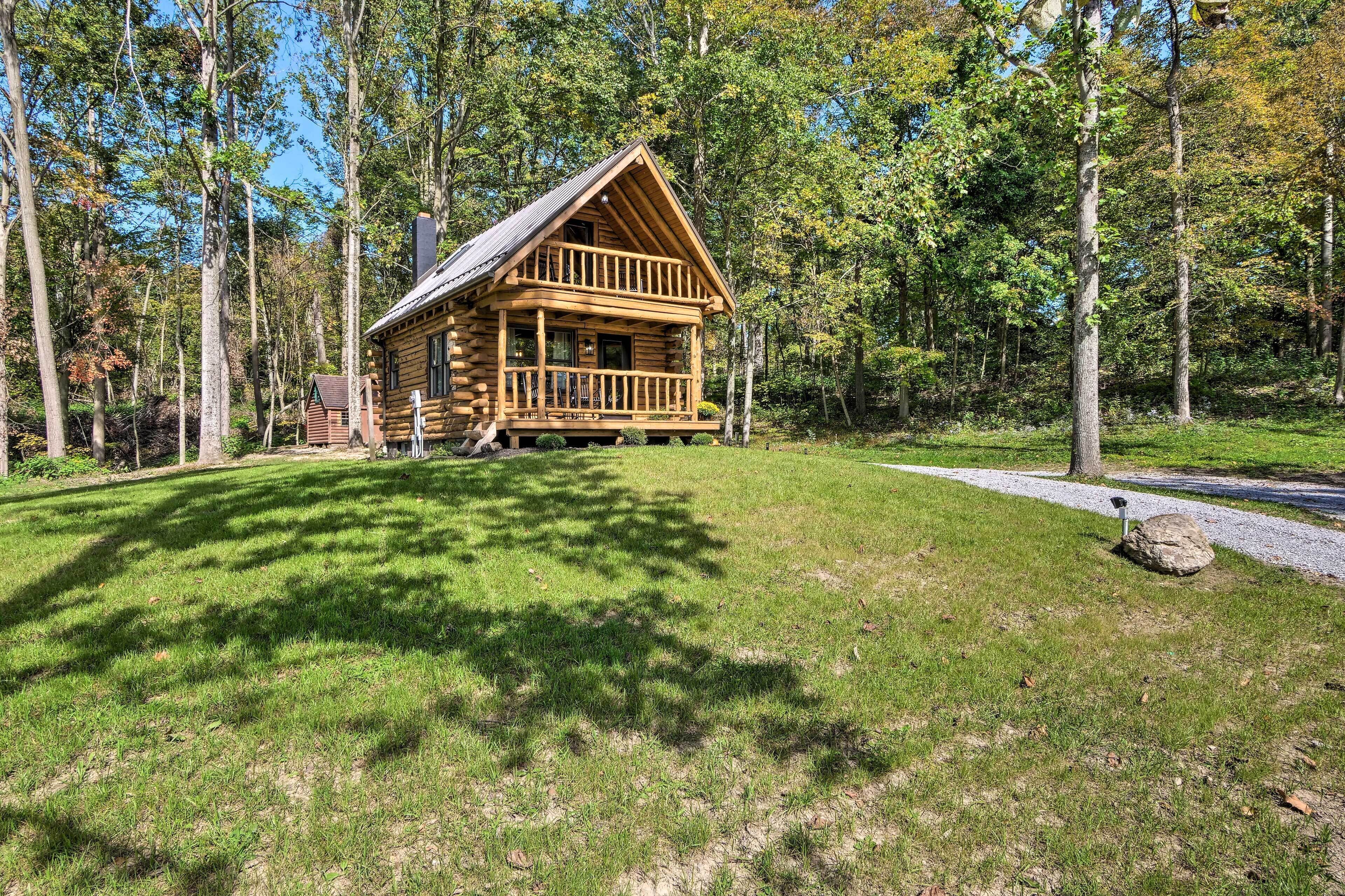 A log cabin with a porch, surrounded by a forest.