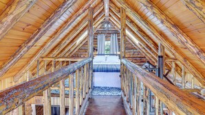 Un intérieur en bois avec un plafond haut et un escalier central menant à un espace aménagé pour dormir.