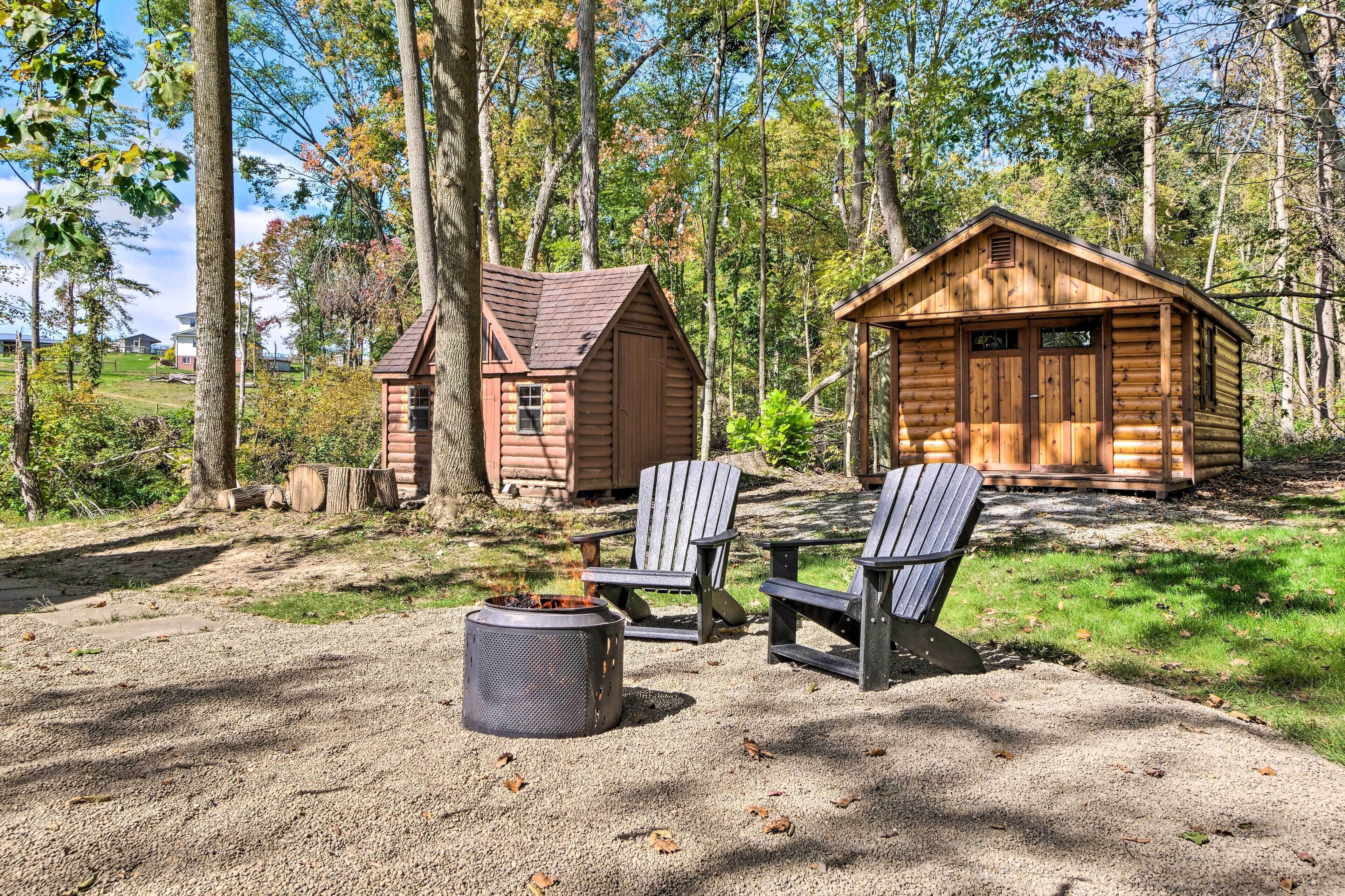 Un chalet rustique avec un foyer et des fauteuils Adirondack, situé dans un cadre forestier.