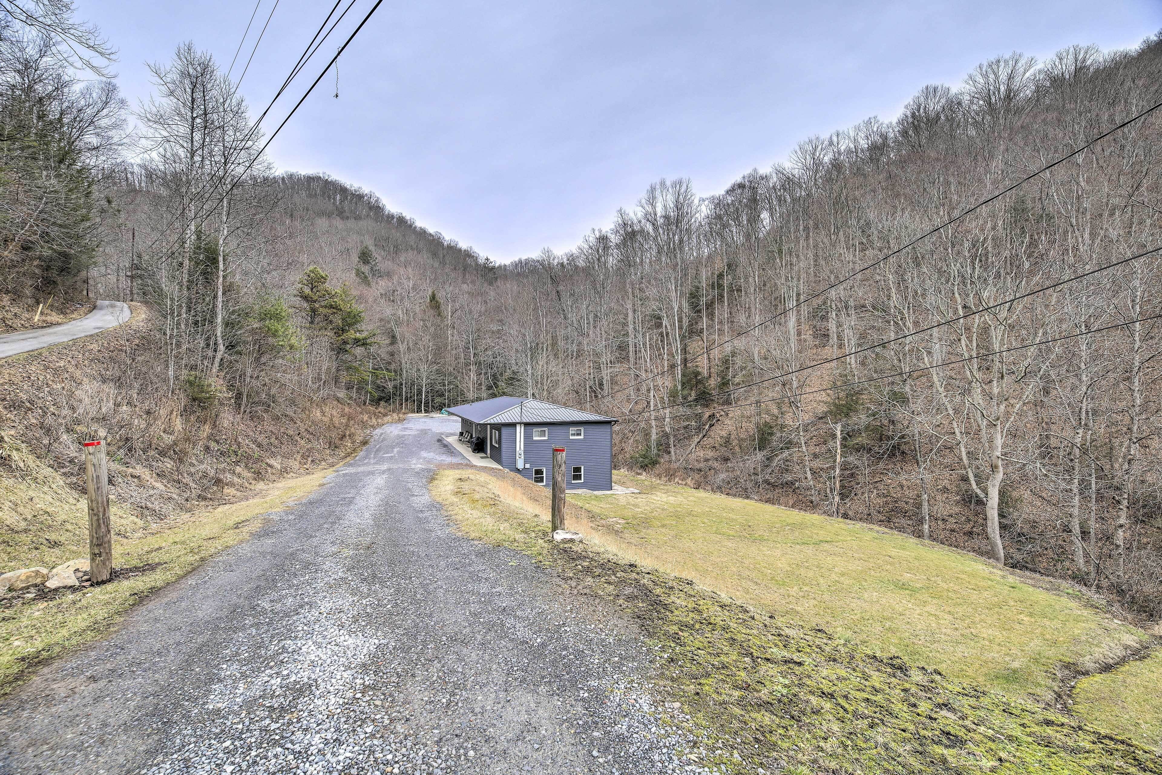A gravel road leading to a small, single-story building with a metal roof, surrounded by a forested area.