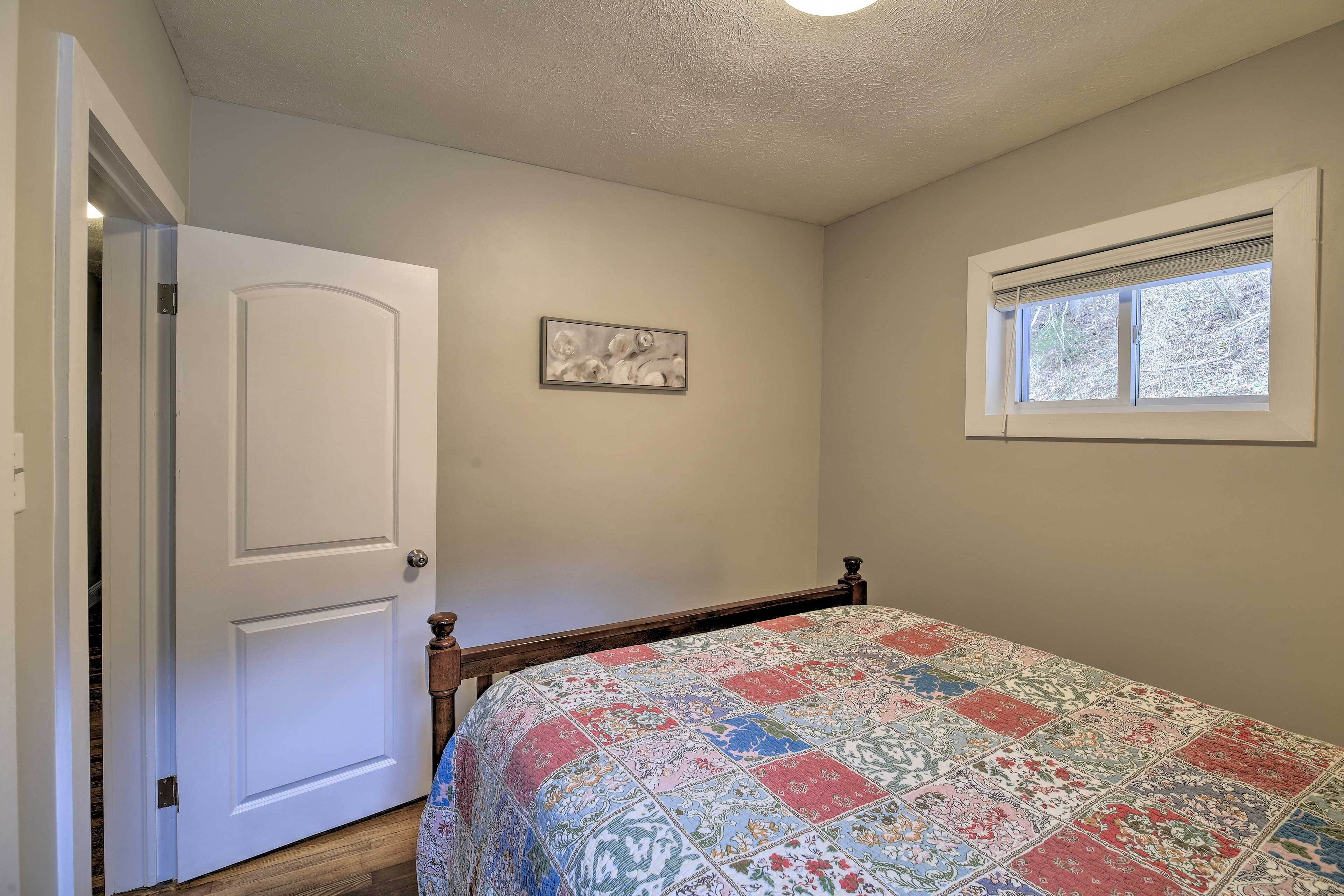 A bedroom with a bed, a door, a window, and a wall-mounted picture.