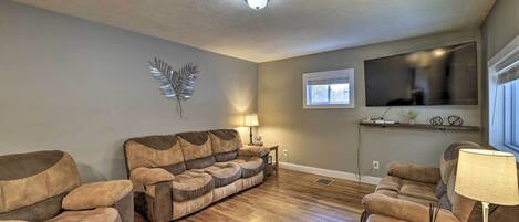 A living room with a brown leather sofa, a wooden coffee table, and a TV mounted on the wall.