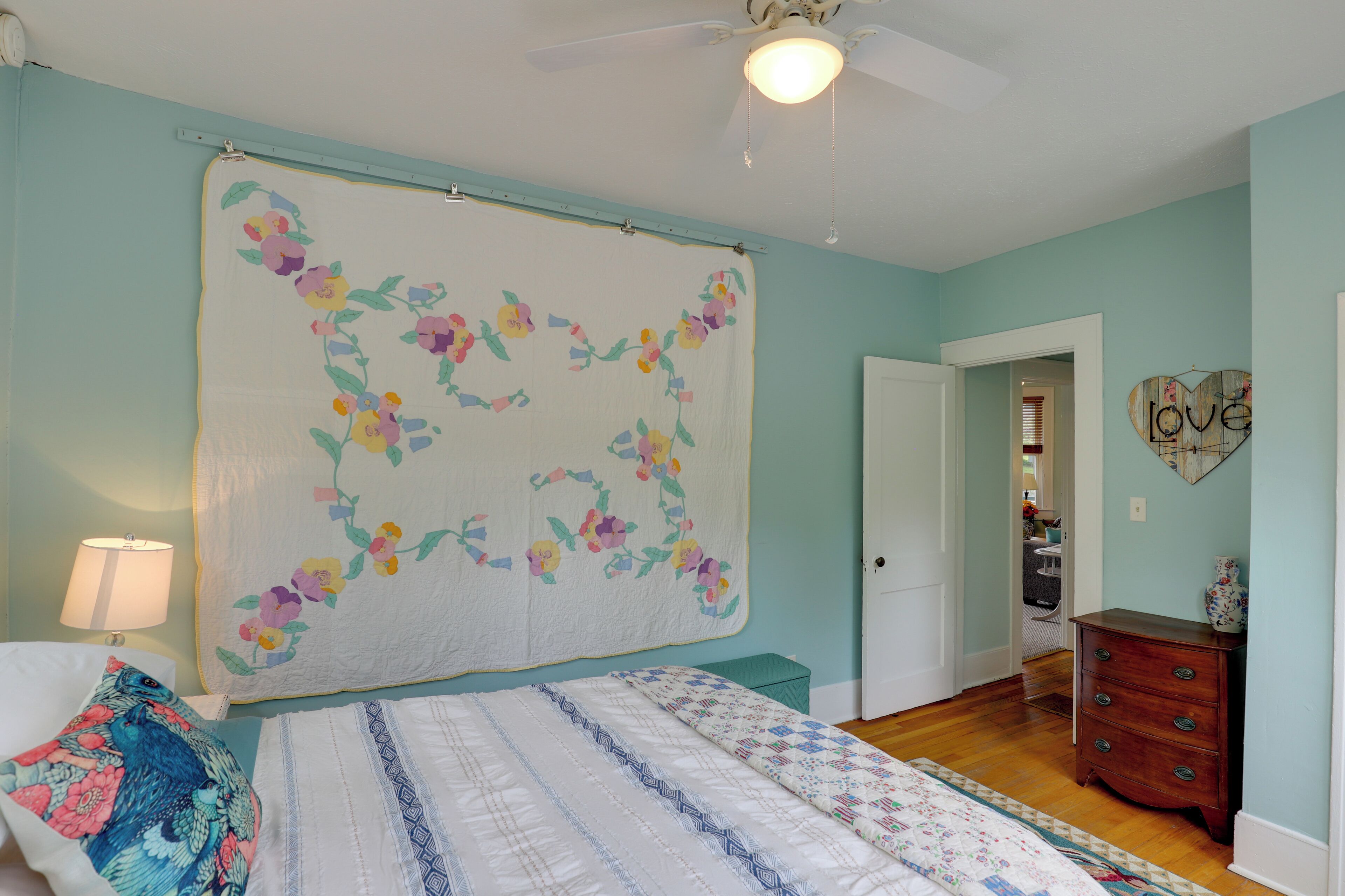 A bedroom with a bed, a dresser, a nightstand, a lamp, and a wall with a floral design.