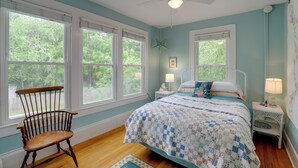 A bedroom with a bed, a chair, two bedside tables, and a ceiling fan.