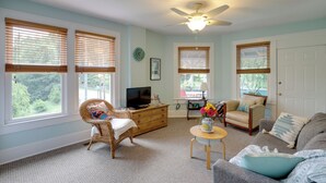 A living room with a television, wicker chairs, a sofa, and a ceiling fan.