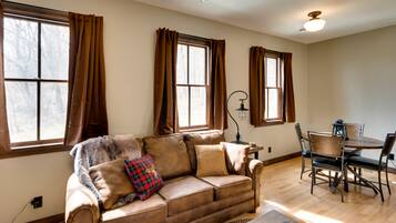 A living room with a brown leather sofa, a dining table with chairs, and large windows with brown curtains.