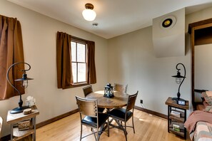 Un coin repas chaleureux avec une table et des chaises en bois, une petite table d’appoint avec une lampe et une fenêtre agrémentée de rideaux.