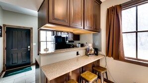 A kitchen with wooden cabinets, a countertop, and three stools. - Pet-friendly Blue Mounds Vacation Rental w/ Yard! (Blue Mounds)