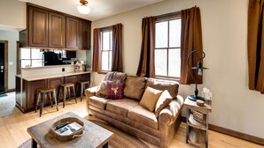 A cozy living room with a brown leather sofa, wooden coffee table, and a kitchen area with wooden cabinets and a black refrigerator. - Pet-friendly Blue Mounds Vacation Rental w/ Yard! (Blue Mounds)