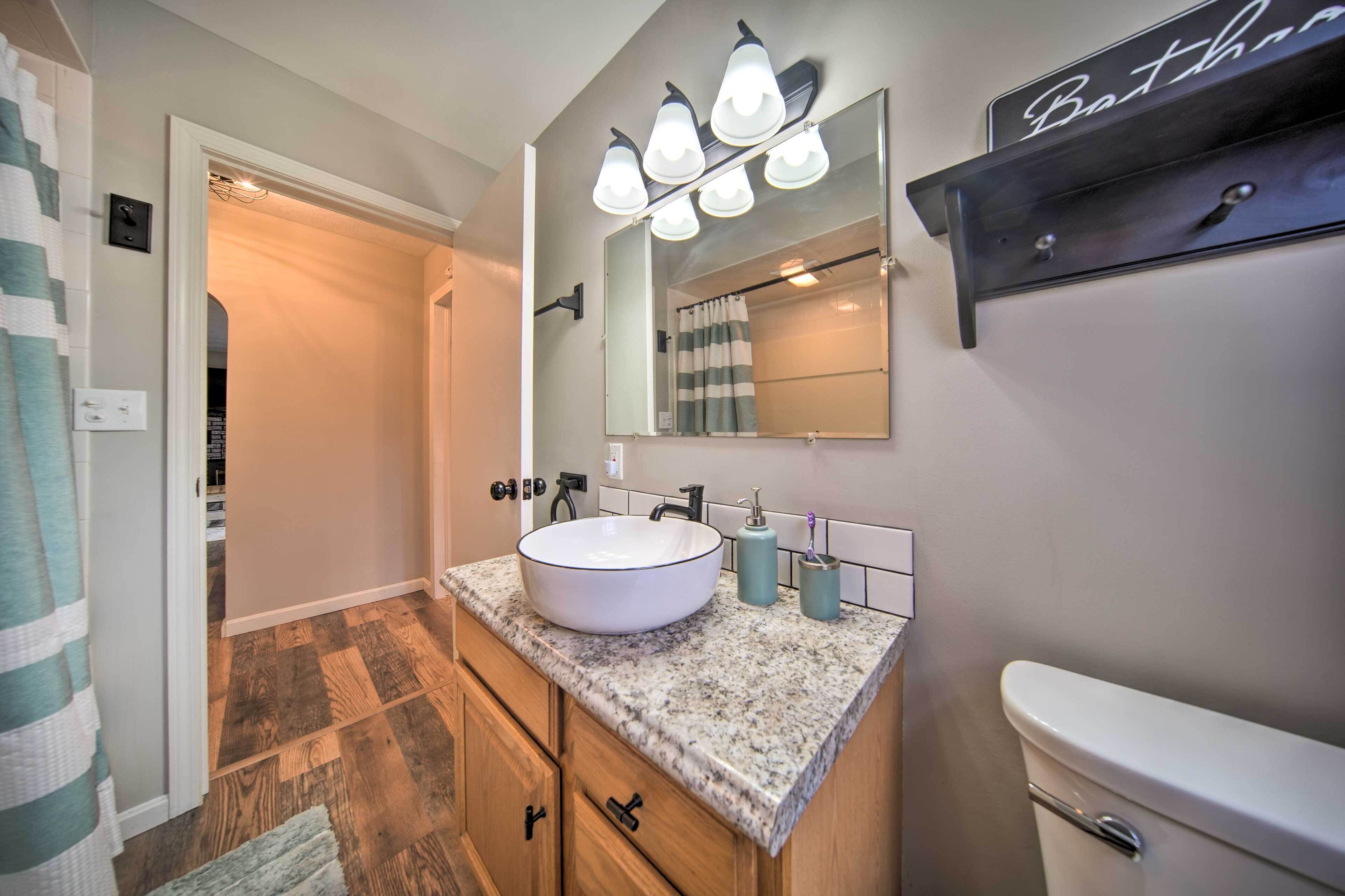 A bathroom with a white sink, a mirror, and a toilet. There is a towel rack and a shelf above the mirror.